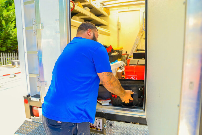 technician in blue shirt grabbing tools from work truck