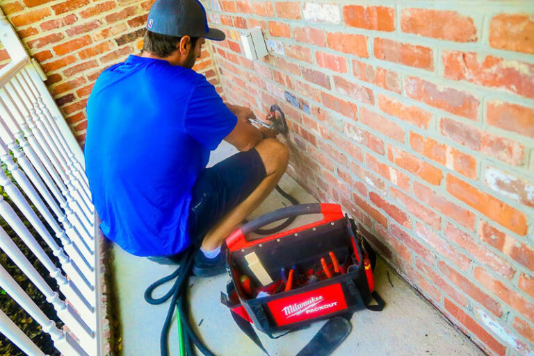 technician in blue shirt repairing a hose bib on side of red brick house